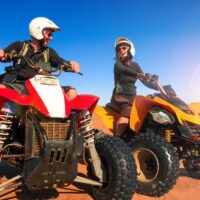 Happy couple of quad bikers laughing joyful, cheerful and fresh. Young active caucasian couple in outdoor activity driving quad ATV in Namib desert sunrise or sunset, Namibia, Africa.